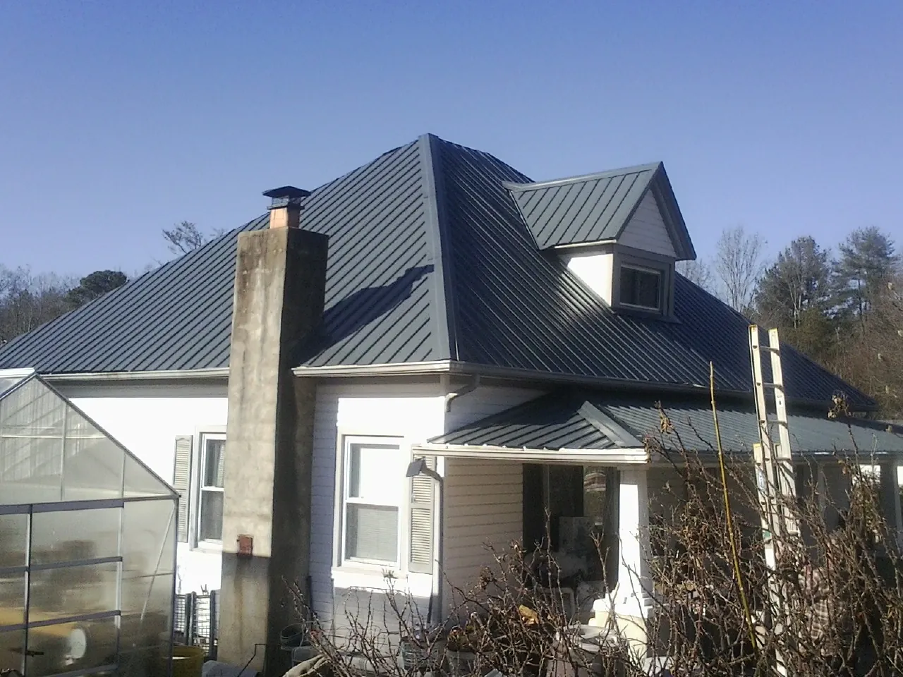 Dark blue standing seam metal roof on a white farmhouse with dormer — Slate & Tile Roof Repair by Roofing Brothers in Clovis